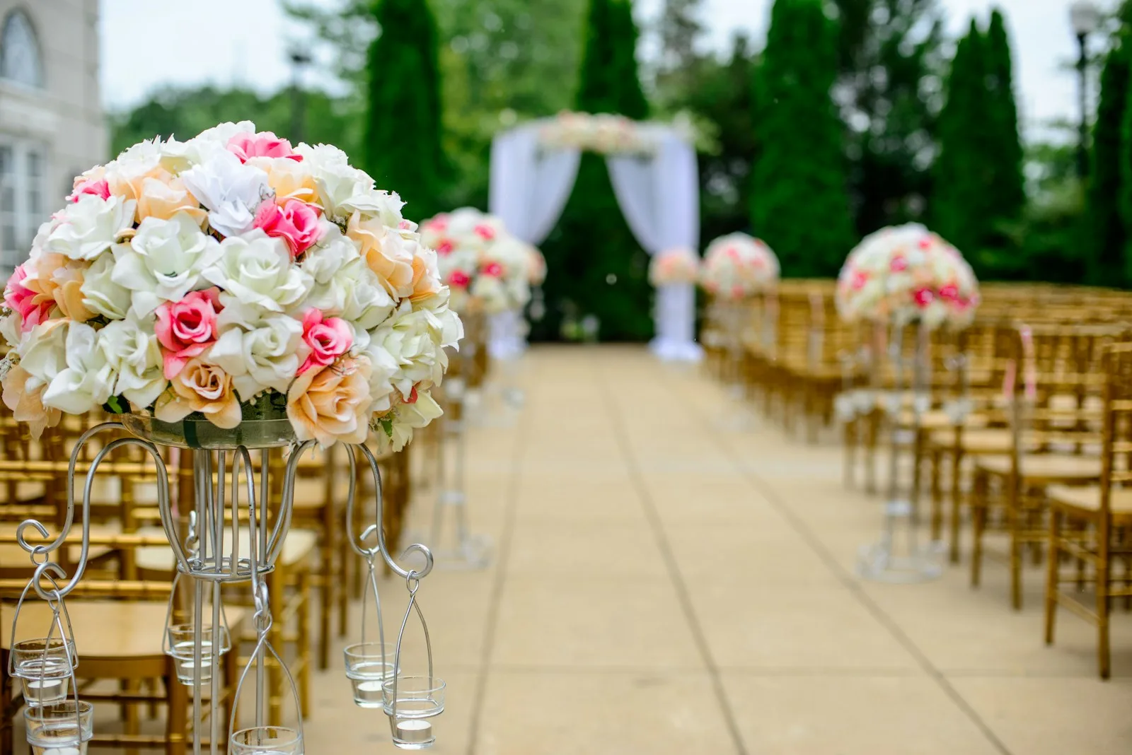 Elegant outdoor wedding ceremony aisle with floral arrangements and golden chairs
